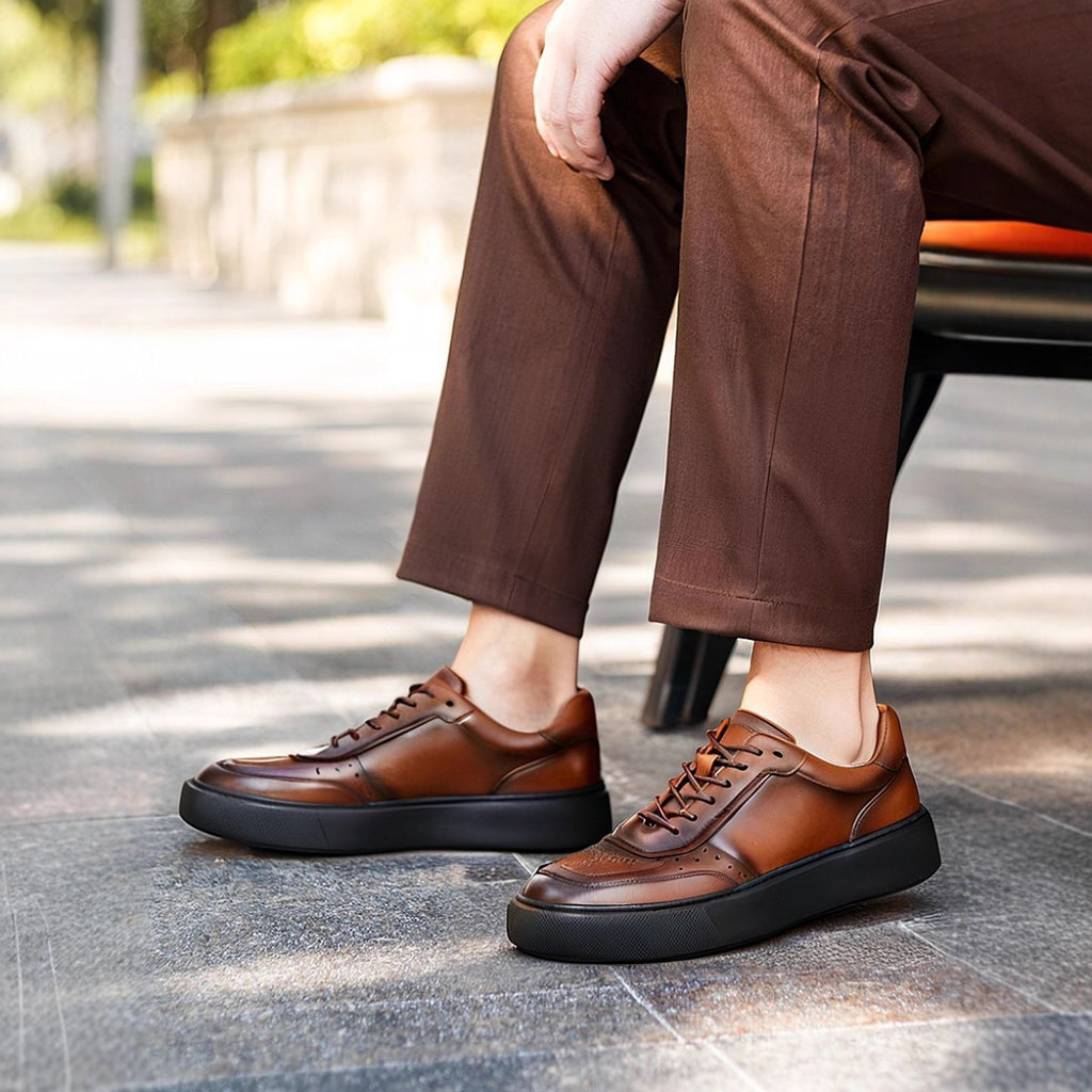 Brown leather lace-up sneakers with perforated toe and chunky black sole, worn outdoors.