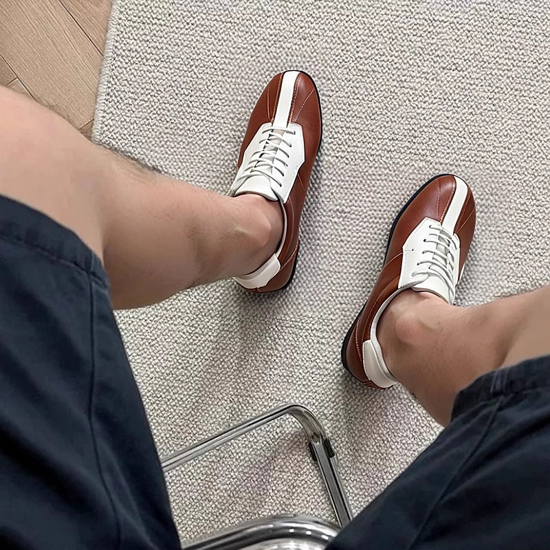Brown leather sneakers with white laces and side panels, worn with dark trousers.