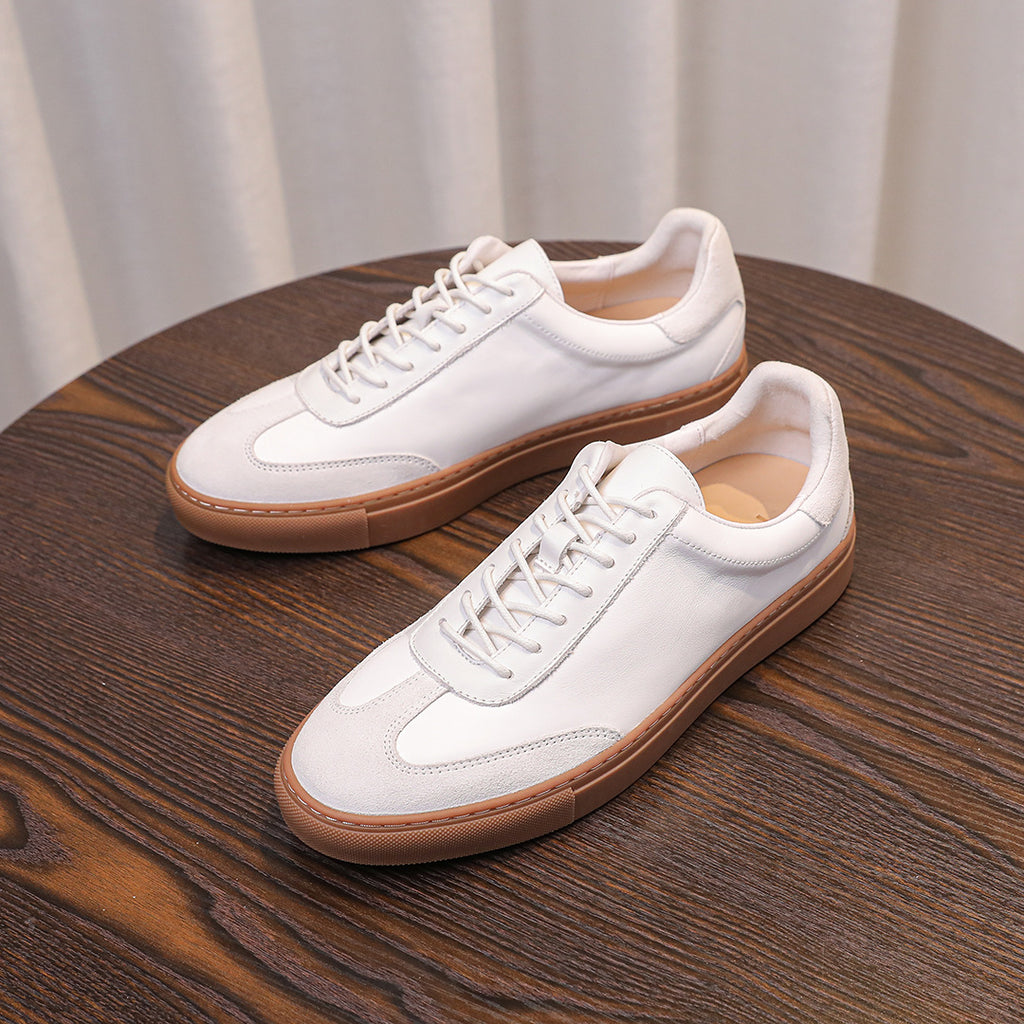 Two white leather sneakers with tan soles on a wooden table