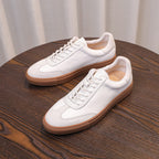 Two white leather sneakers with tan soles on a wooden table