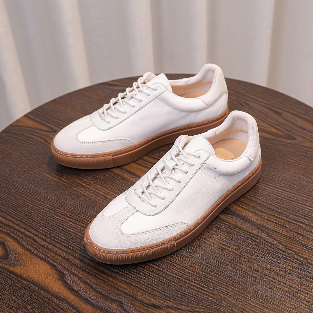 Two white leather sneakers with tan soles on a wooden table